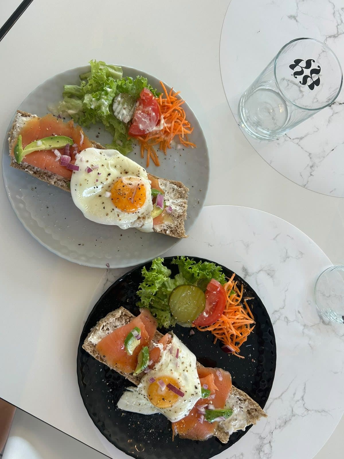 Un toast à l'avocat surmonté d'un œuf poché, servi avec du saumon fumé et une salade.