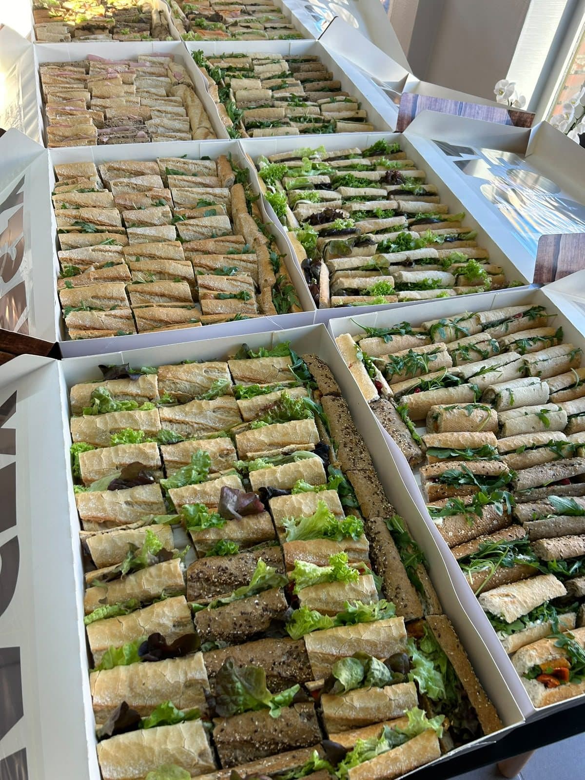 De longs plateaux de mini-sandwichs garnis, alignés sur un comptoir.